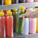 A hand holding a 16 oz. round clear juice bottle with yellow liquid.