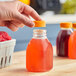 A hand holding a Square Milkman juice bottle filled with orange liquid and a lid.