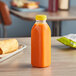 A 16 oz. Square Milkman PET clear juice bottle with a yellow lid on a table.
