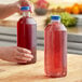 A hand pouring red juice into a square PET juice bottle on a counter.