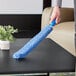 A hand using a Lavex blue microfiber duster sleeve to dust a black surface.