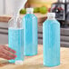 A hand pouring blue juice into a 32 oz. clear square juice bottle on a kitchen counter.