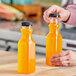 A hand pouring orange juice into a 12 oz. square PET clear carafe juice bottle.