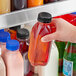 A hand holding a 12 oz. Square Milkman PET clear juice bottle with a black lid full of liquid.