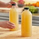 Two people holding 32 oz square PET juice bottles filled with yellow liquid.