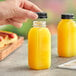 A hand holding a bottle of orange juice with a black lid.