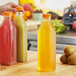 A person's hand holding a tall square clear juice bottle with orange liquid.