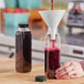 A hand pouring liquid into a 12 oz. clear square juice bottle with a black lid.