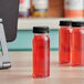 4 oz. Round PET Clear Energy Bottles filled with red liquid on a counter in a juice bar.