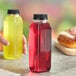 A person holding a square clear juice bottle filled with red liquid next to a bagel.