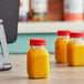 Three 4 oz. square PET bottles of orange juice with red lids on a counter.