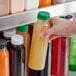 A hand holding a 12 oz. round PET clear juice bottle with dark green liquid.
