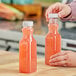 A person pouring orange juice into a 12 oz. square PET clear carafe juice bottle.