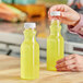 A hand pouring yellow liquid into a 12 oz. square PET clear carafe juice bottle.