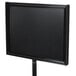 An Aarco black rectangular aluminum hostess/teller sign with a metal frame on a black pole.