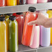 A hand holding a round clear rPET juice bottle filled with yellow liquid.