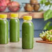 Three green juice bottles on a counter with fruit.