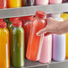 A hand holding a 16 oz. round clear rPET juice bottle with a red lid.