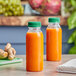 Two 8 oz. round PET clear juice bottles with green lids filled with orange juice on a counter.
