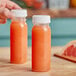 A hand holding a 4 oz. round clear PET bottle of orange liquid.