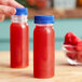 A hand holding a round clear plastic bottle of red raspberry juice.