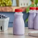 A close-up of a white round PET juice bottle with a red cap full of purple liquid.