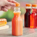 A hand holding a 10 oz. square PET clear carafe juice bottle of orange juice.