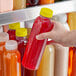 A hand holding a clear round PET juice bottle with a yellow lid full of yellow liquid.