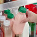 A hand holding a 12 oz. Square Milkman PET Clear Juice Bottle with a dark green lid full of pink liquid.