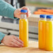 A person's hand opening a yellow 12 oz. round PET juice bottle.