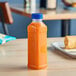 A 16 oz. square PET clear juice bottle with a blue lid filled with orange juice on a table.