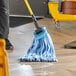 A person mops the floor with a Lavex blue microfiber tube mop with a blue headband.