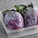 A plastic container holding two whole red cabbage heads.