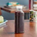 A 15.2 oz. Square PET clear juice bottle with clear liquid sitting on a table.