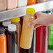 A hand holding a 12 oz. round PET clear juice bottle with a yellow lid.
