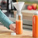 A person pouring orange juice into a round clear bottle.