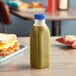 A 16 oz. clear square PET juice bottle with a green liquid on a table.