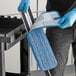 A person in blue gloves using a Lavex blue and white microfiber mop pad to clean a kitchen counter.