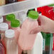 A person holding a 12 oz. square clear plastic bottle of pink juice with a lime green lid.