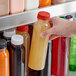 A hand holding a 12 oz. round PET clear juice bottle with a red lid.