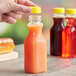 A person holding a 10 oz. square PET clear carafe juice bottle with a yellow lid.