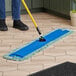 A person using a yellow and blue Lavex microfiber mop to clean a floor.