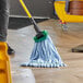A person in a yellow room using a Lavex Blue Microfiber Tube Mop with a green handle to clean a floor.
