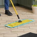 A person using a Lavex 24" microfiber dust mop with a yellow handle on a tile floor.