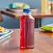 A 15.2 oz. square clear PET juice bottle with red liquid and a blue lid on a table.