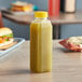 A 16 oz. tall square PET clear juice bottle with yellow liquid on a table.