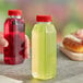 A hand holding a 10 oz. square clear plastic juice bottle with a red lid.