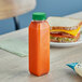 A 12 oz. clear rPET juice bottle with a green lid next to a sandwich.