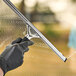 A person's gloved hand using an Ettore Master stainless steel squeegee to clean a window.