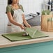 A woman in an apron cutting green SatinWrap tissue paper on a counter.